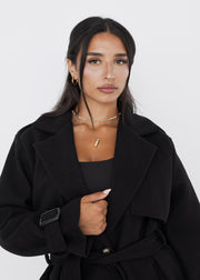 Trench noir ample à ceinture — détail du col et des revers.