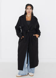 Trench noir ample à ceinture — vue portée de face.