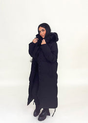 Parka noire capuche fourrure — vue portée en pied, mains dans les poches latérales