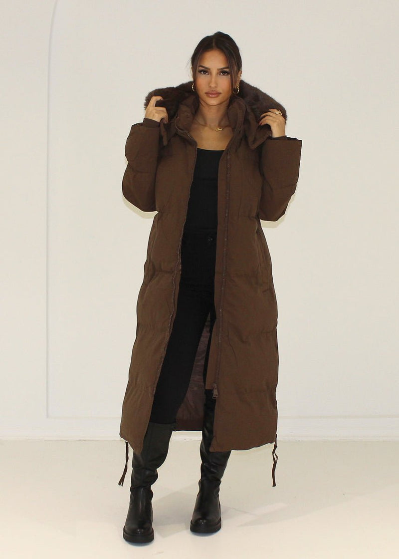 Parka brune capuche fourrure — vue portée en pied, capuche relevée, bottes noires