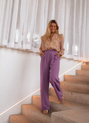 Chemisier fluide à motifs dorés porté par une femme, silhouette entière, pantalon violet, escalier