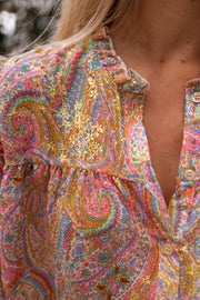 Chemisier fluide à motifs dorés porté par une femme, vue rapprochée, col V, motif paisley